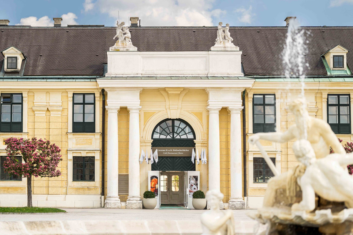 Eingang zum Café Restaurant im Schlosspark Schönbrunn in Wien. Im Vordergrund rechts ist leicht unscharf ein Springbrunnen 